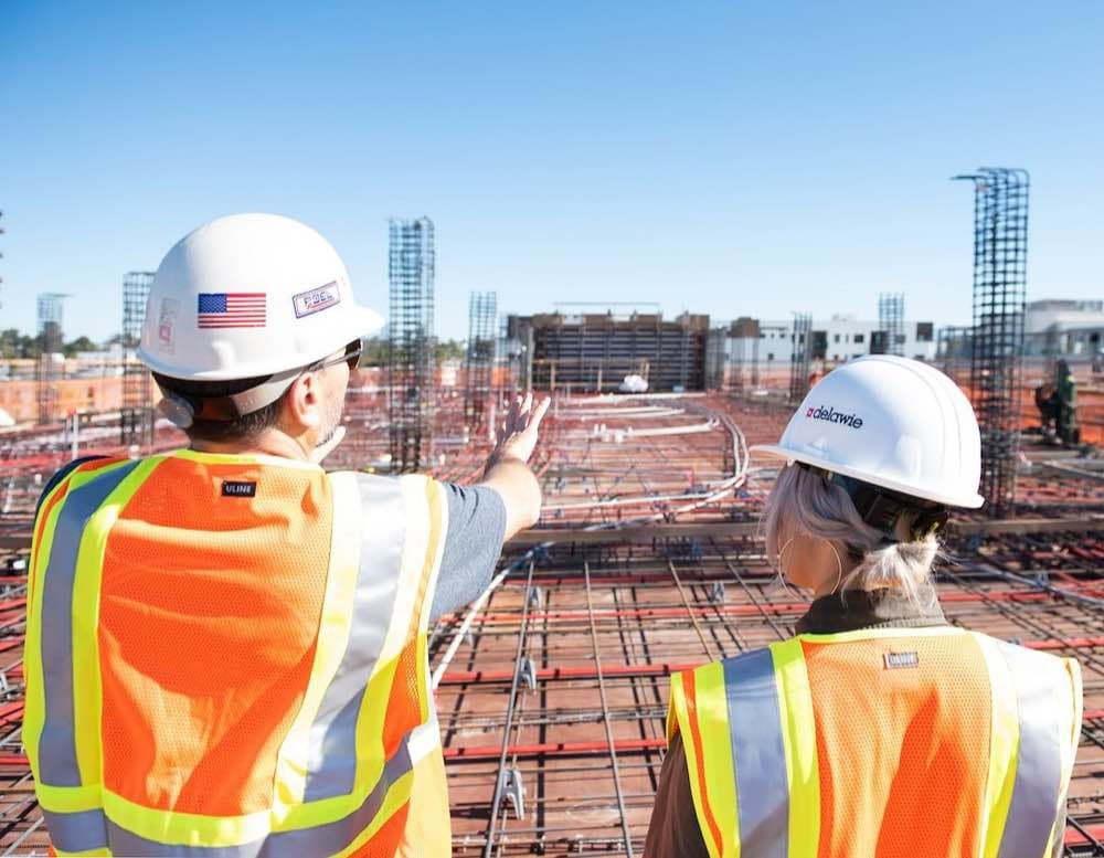 Two people looking out over the rebar deck of a building under construction